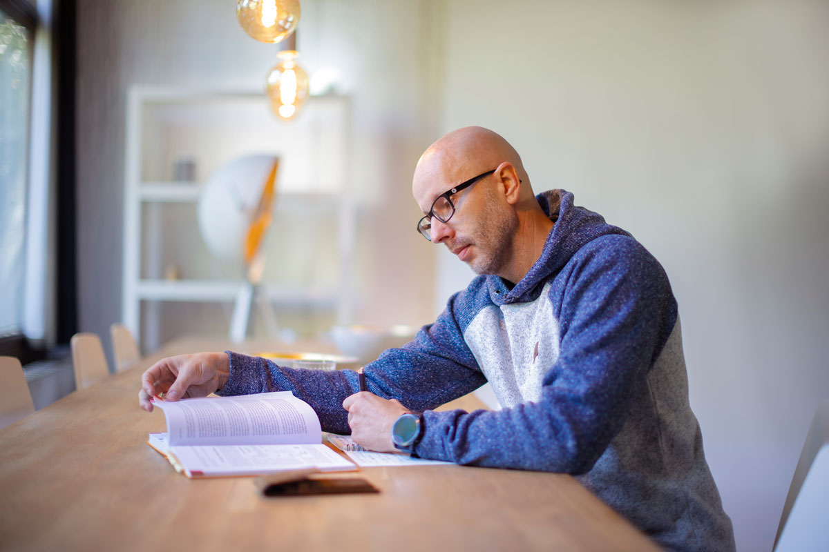 Foto von Axel Hillebrandt - sitzend an einem Tisch - liest ein Buch und erstellt Notizen. Ambiente Workingroom.